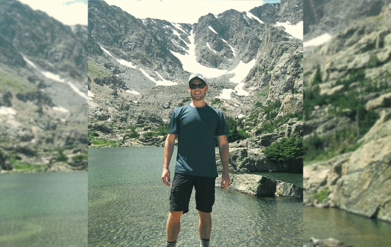 A man standing by a serene mountain lake, surrounded by breathtaking natural beauty.